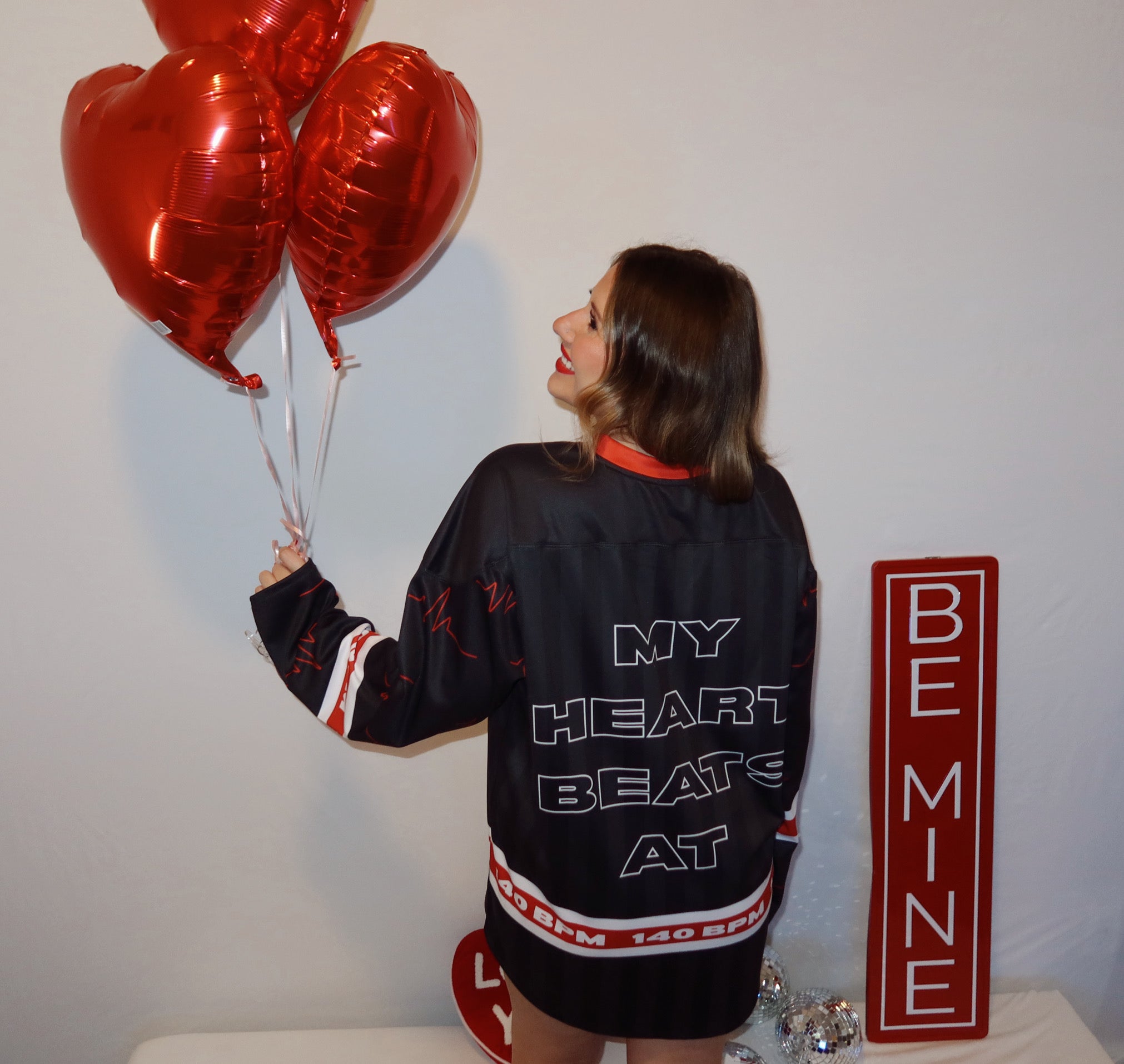 Model is showing the back of a red and black dubstep rave hockey jersey that says my heart beats at 140 BPM.