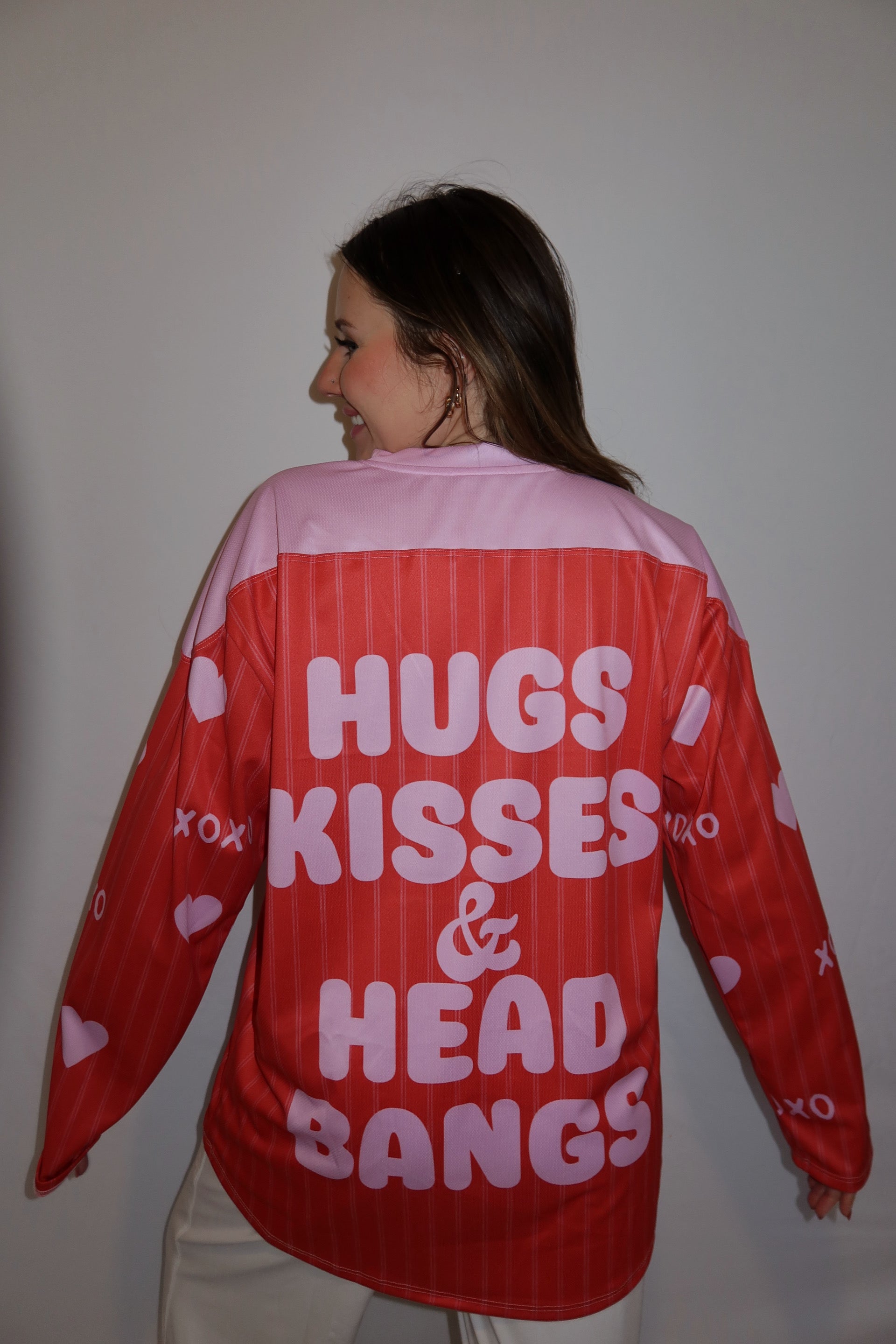 Person showing the back of the hockey jersey. It says hugs, kisses, and head bangs.