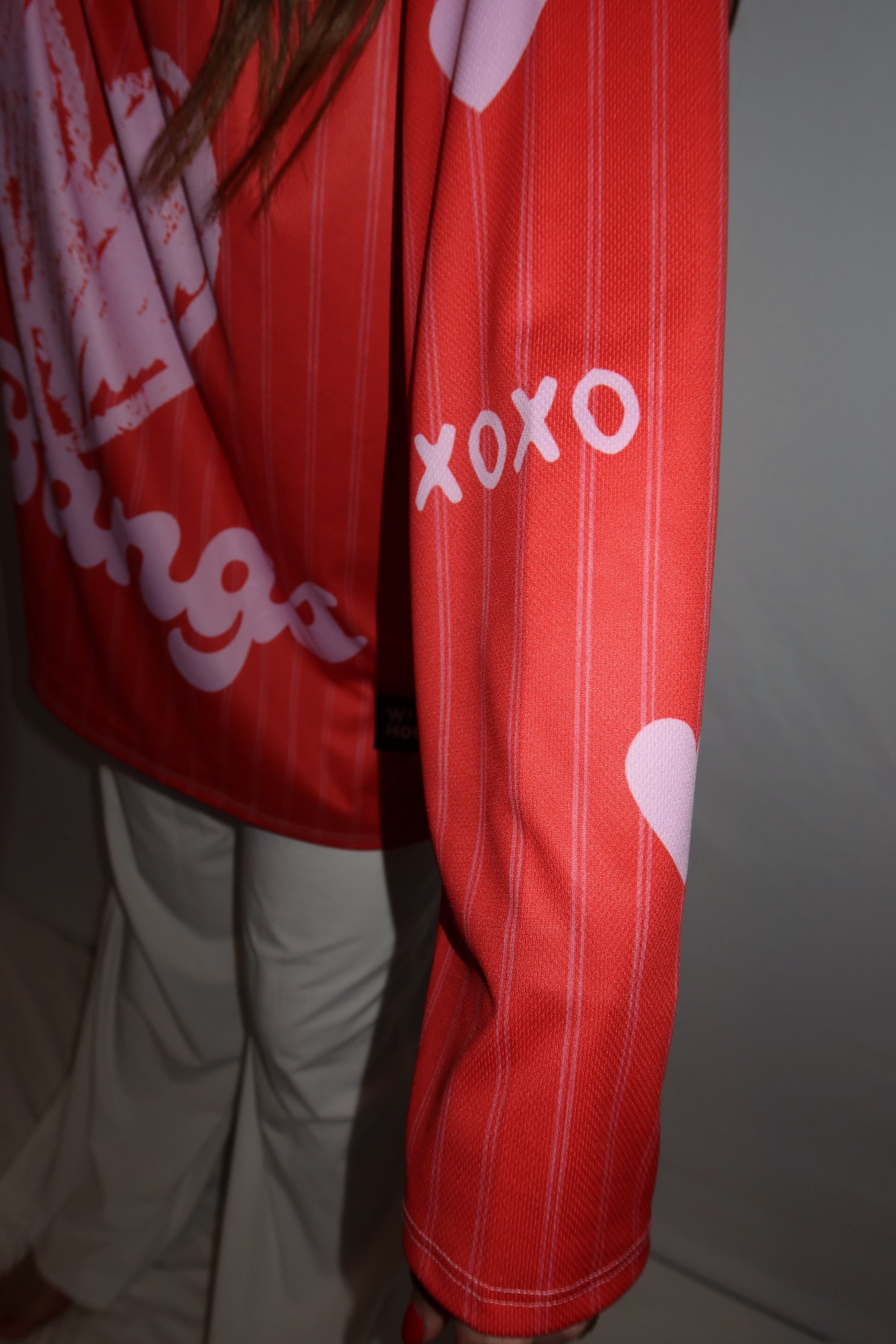 Person showing the sleeve of the red and pink rave hockey jersey where it says XOXO in pink. 