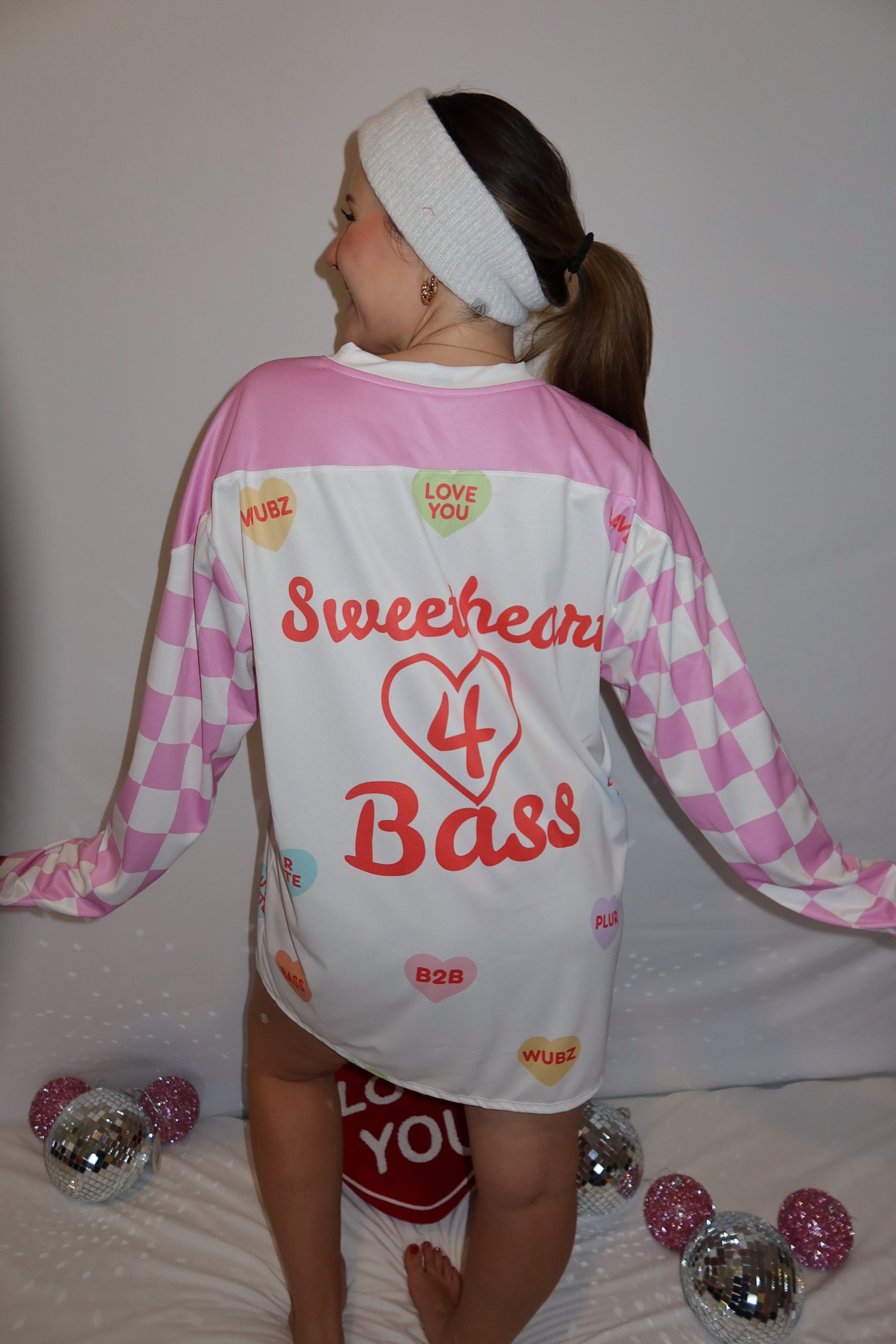 Person showing back of a rave hockey jersey. It's pink checkered on the sleeve and says sweetheart 4 bass on the back. 