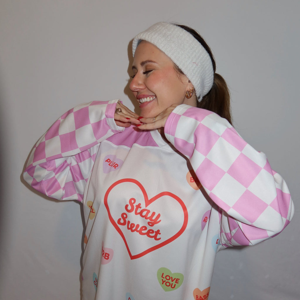 Person smiling and showing front of rave hockey jersey. It says stay sweet with sweet hearts all on it and rave terms like B2B, Wubz, and Drop It. 